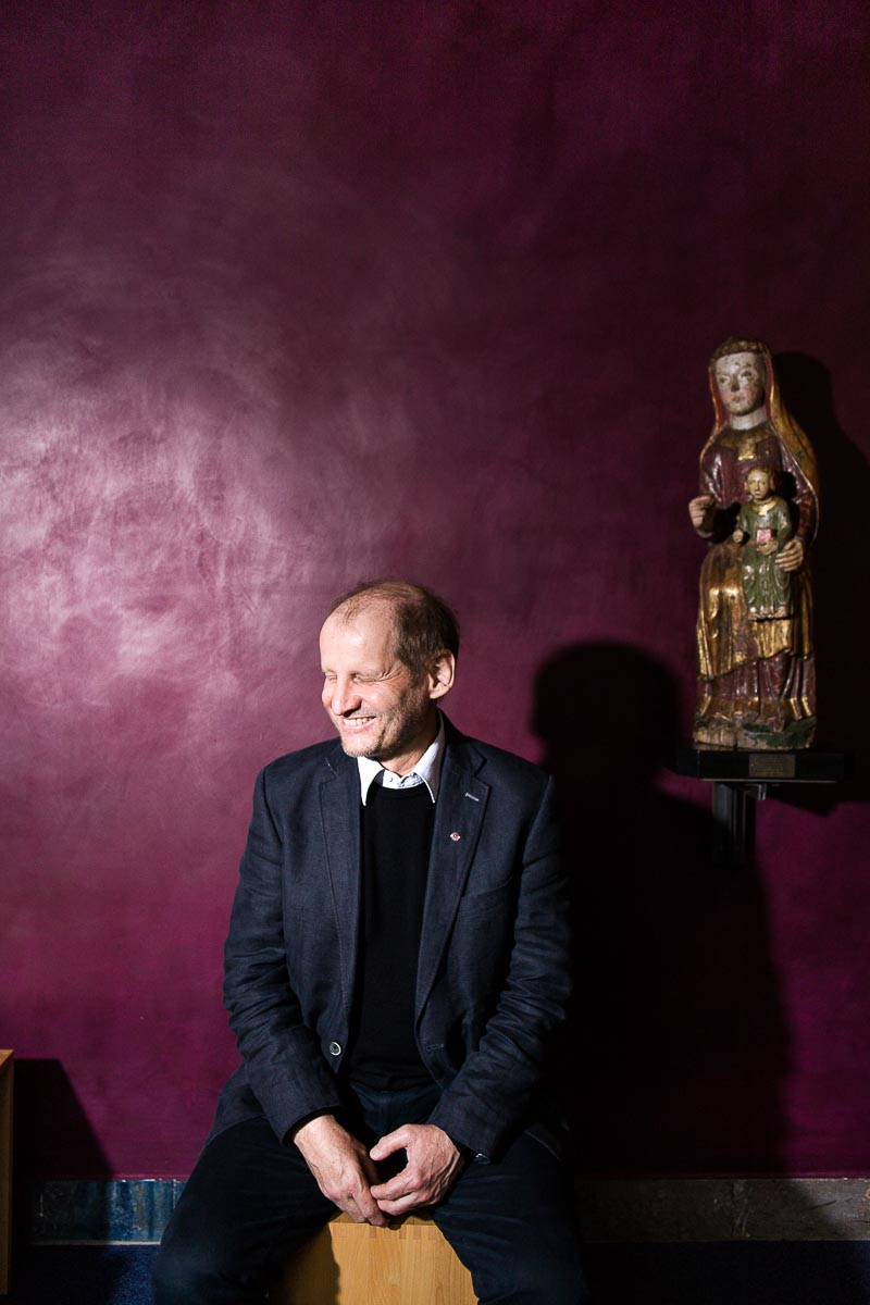 Portraitaufnahme Monsignore Pirmin Spiegel von Misereor sitzend unter einer Madonna in einer Kapelle